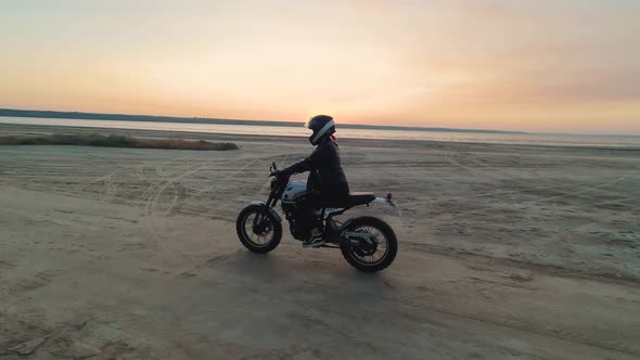 Young Stylish Woman Motorcyclist Driving Her Motorcycle in the Desert Road During Sunset