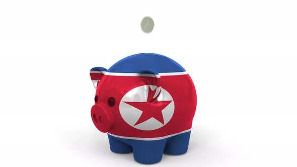 Coins Fall Into Piggy Bank Painted with Flag of North Korea