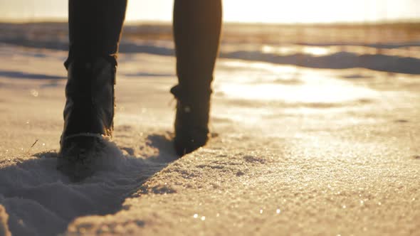 Female Feet in Black Boots Winter Walking in Snow at Sunset