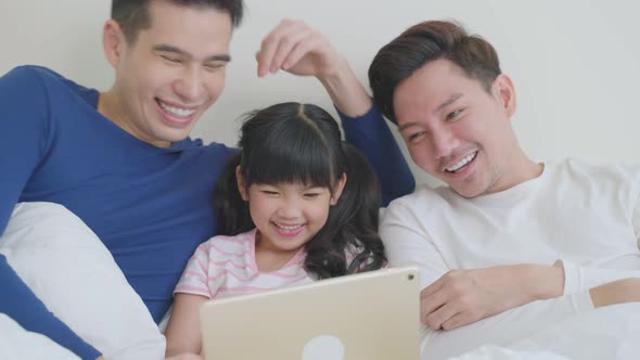 Asian attractive LGBTQ gay family teach girl kid using tablet on bed.