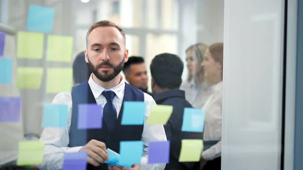 Pensive Fashion Businessman Having Brainstorming Stick Colorful Stickers to Glass Board