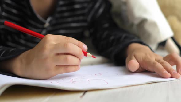 Small Child Boy Is Painting Picture Using Red Pencil in Album, Hands Closeup.