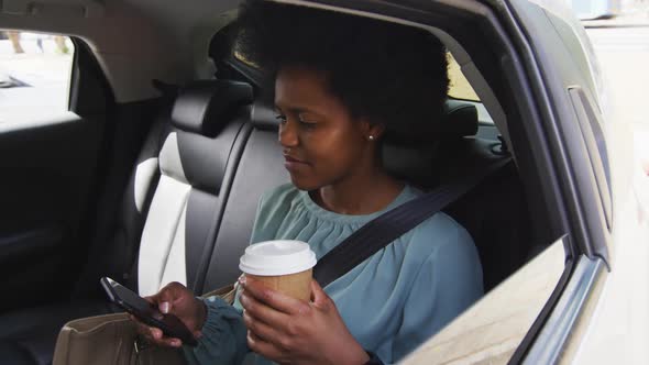 African american businesswoman using smartphone and holding takeaway coffee in car