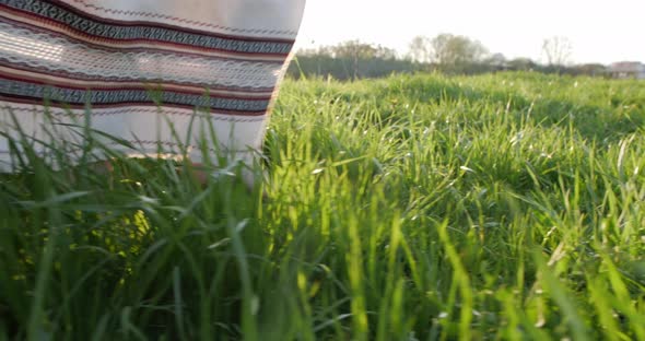 A Girl in an Embroidered Dress Walks on the Grass at Sunset