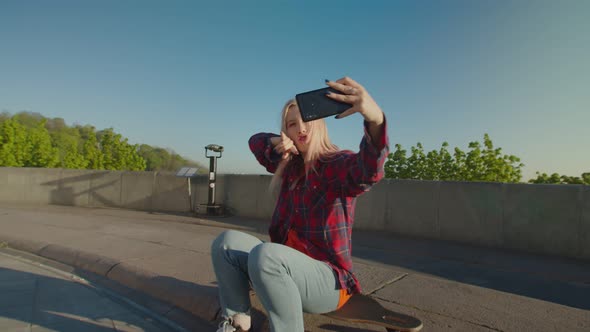 Cute Woman Skater Sitting on Skateboard Filming Video on Cellphone at Dawn