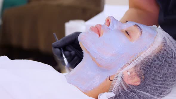 Close-up, Cosmetician in Black Gloves, Applies Blue Cosmetic Face Mask with Special Brush To Female