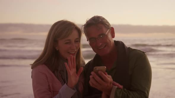 Active senior couple using phone on beach