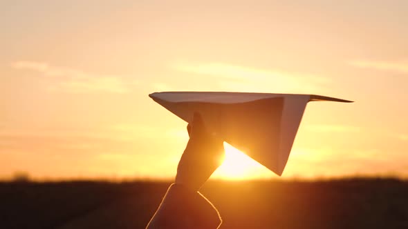 Woman Launches Paper Airplane Against Sunset Background