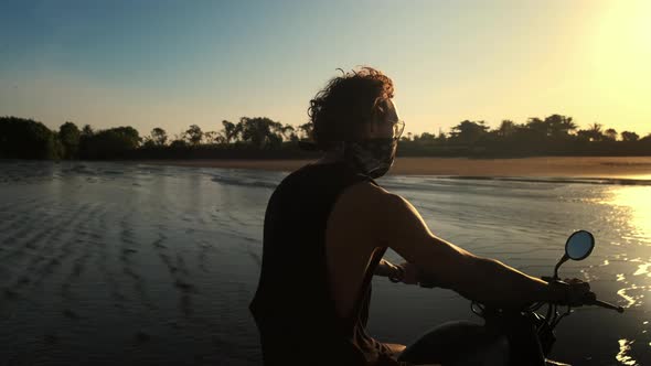 Motorcyclist is Riding on Ocean Coast at Sunset Time