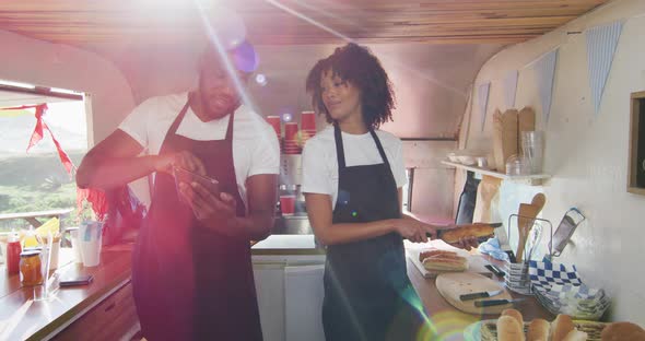 African american couple wearing aprons using digital tablet and preparing hot dogs in the food truck