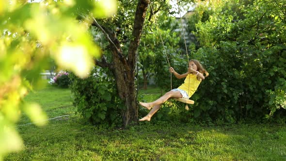 Happy barefoot laughing child girl swinging on a swing in sunset