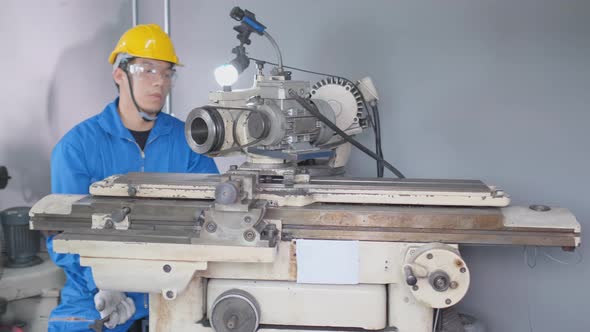 Wide shot of Asian factory worker with yellow hardhat and blue uniform work with machine