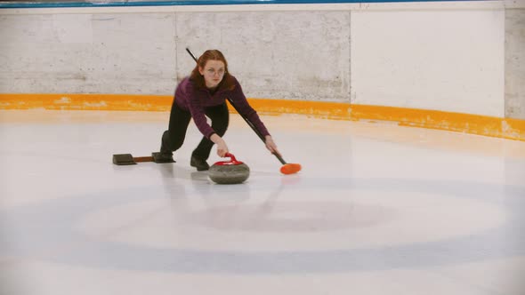 Curling - a Woman in Glasses Pushes Off on the Ice Field with a Granite Stone Holding a Brush