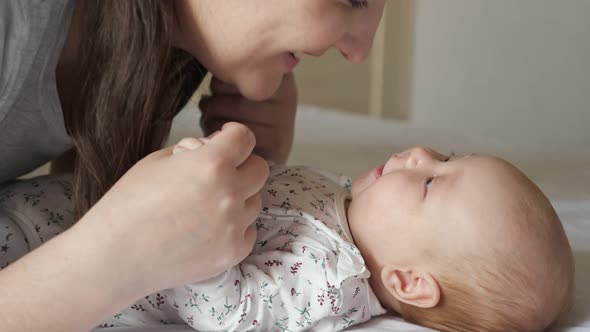 Happy Mother Kisses Plump Cheeks of Newborn Daughter