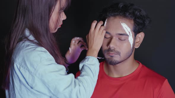 Make up artist applying white prosthetic insert on man's face to make a Halloween mask