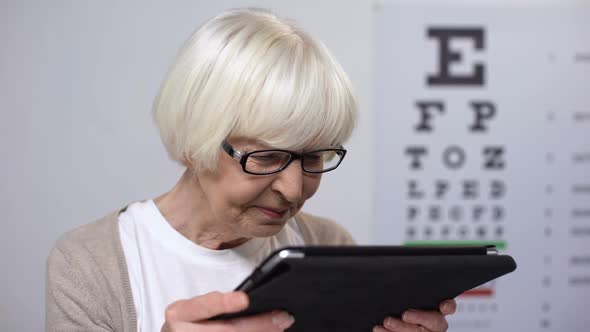Wrinkled Elderly Woman Holding Tab and Trying to Read, Unhappy With Poor Sight