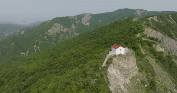 High angle aerial shot of a small building surrounded with forested hills.