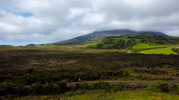 Aerial shot of people hiking the Mount Pico, going on the dirt road. Pico Island in the background.