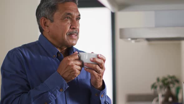 Senior mixed race man in kitchen drinking coffee