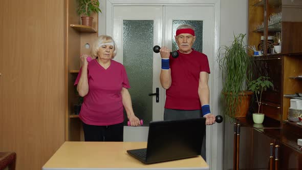 Senior Elderly Couple Watching Online Workout Exercises on Mobile Phone and Training with Dumbbells