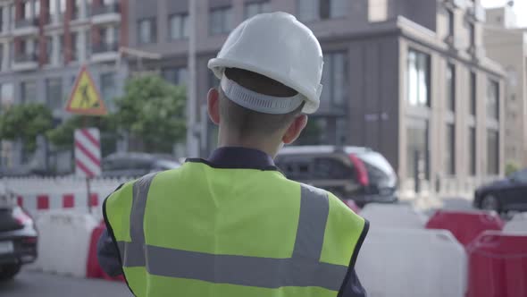 Little Boy Wearing Business Suit and Safety Equipment and Constructor Helmet Standing on a Busy Road