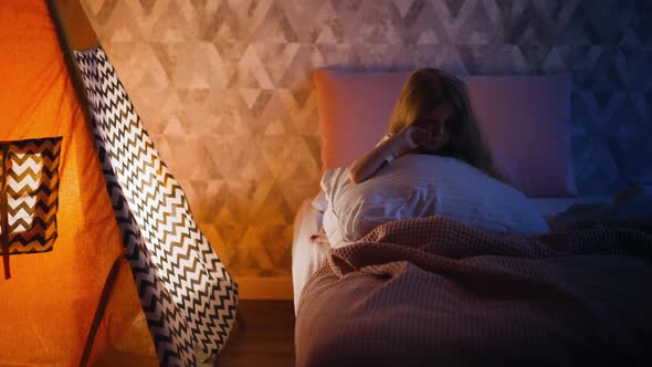 Girl Hugging Pillow Wipes Away Tears Sitting Alone on Bed