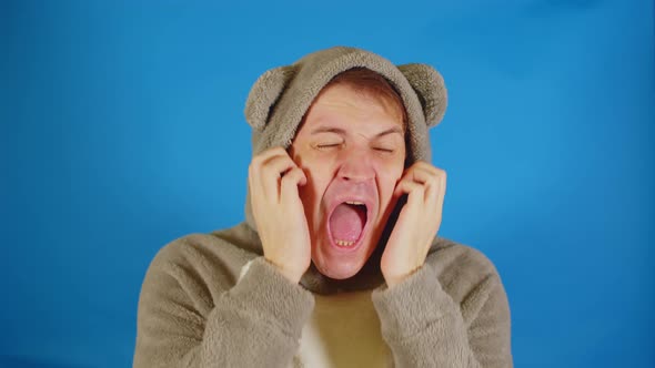 Man in Hoodie with Ears Scratches His Face Standing on Blue Background