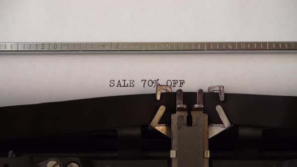 Typing phrase SALE 70% OFF on retro typewriter. Close up.