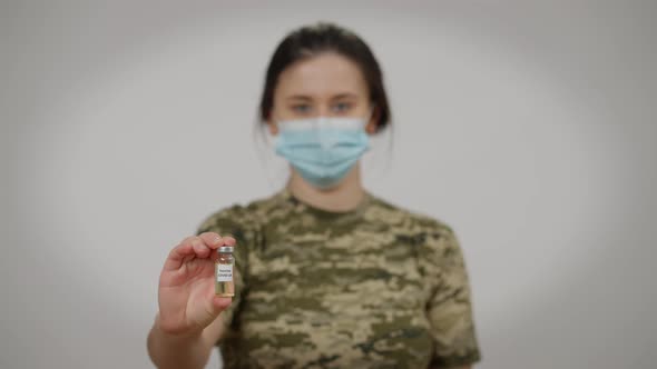 Blurred Female Soldier in Covid Face Mask Posing with Coronavirus Vaccine Jab at Grey Background