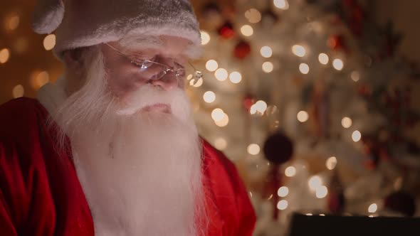 Closeup Side View of a Real Santa Claus Working with a Laptop at Night with Glasses in the Light of