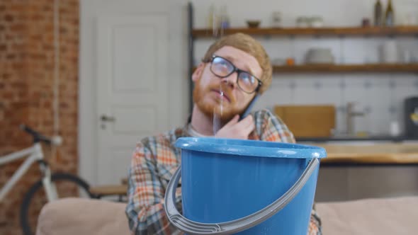 Portrait of Man Calling on Phone Holding Bucket During Leak in Apartment