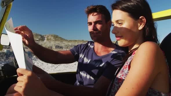 Caucasian couple sitting in beach buggy by the sea reading a map