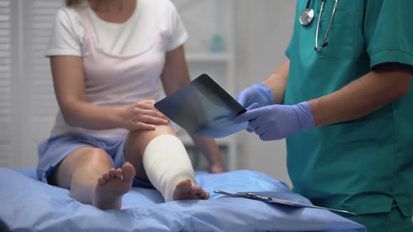 Surgeon Informing Knee Bone X-Ray Result to Female Patient in Elastic Leg Wrap