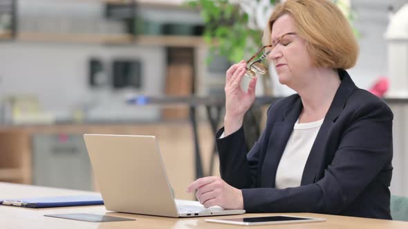 Old Businesswoman with Laptop Having Headache in Office