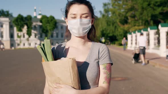 Caucasian Young Pretty Woman Delivery Worker in Medical Mask Walking the Street and Carrying Packet