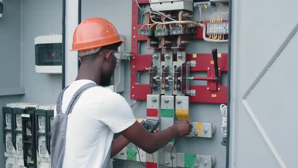 African American Electrician in Safety Helmet and Glasses Checking Voltage in