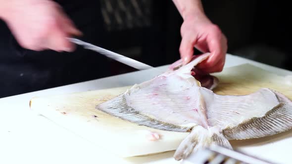 A fish vendor cleans up a nice monkfish with a kitchen knife, over a white cutting board. He cuts th