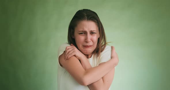 Scared Crying Woman in White Tshirt Hugs Herself on Green