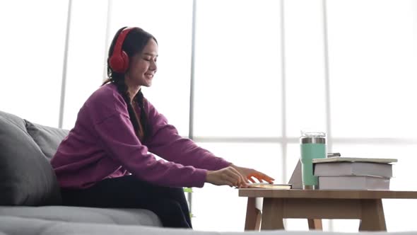 Happy young asian woman relaxing at home sit on sofa holding digital tablet enjoying