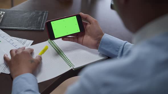 Unrecognizable African American Man Holding Smartphone with Chromakey Green Screen Thinking