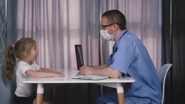 Doctor in Mask Examines Throat of Little Girl in Hospital