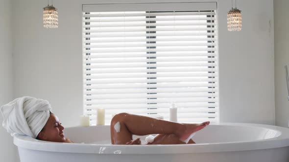 African american woman blowing soap bubbles in the bath tub in the bathroom at home