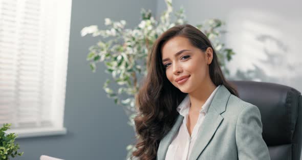 Attractive Corporate Office Worker Sits at Desk in Front of Laptop Screen Looks Into Camera