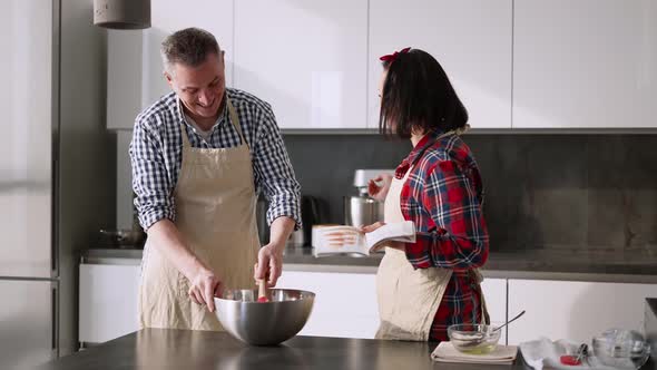 Young Man Preparing Food and Woman Showing Him Something in Recipe Book