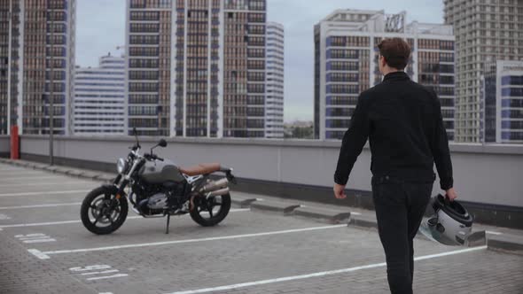 Man Comes to Motorbike and Wears Helmet on Top of the Multilevel Parking