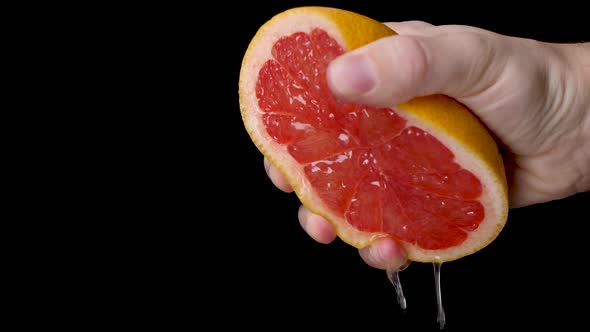 Slow motion squeezing a half cut grapefruit with a white hand with a lot of pressure on a black back