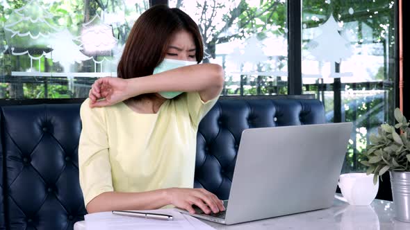 Young Asian businesswoman wearing masks and sneezing by using arms to block virus