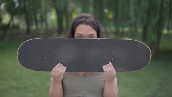 Cheerful Caucasian Little Person Hiding Face with Skateboard Looking at Camera Smiling