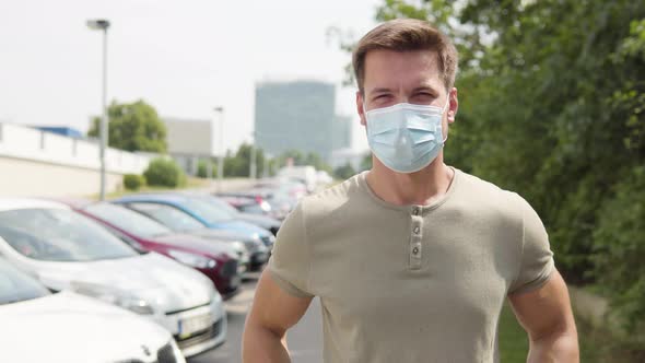 A Young Man Puts on a Face Mask, Looks at the Camera, Then Takes the Mask Off in a Parking Lot