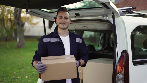 Handsome Smiling Man in Uniform Taking Box Out of Trunk and Looking at the Camera